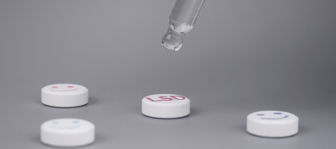 1D-LSD Tablette, auf die mit einer Pinzette eine Flüssigkeit getropft wird, vor einem hellen Hintergrund, hervorhebend die Präzision und Reinheit des Produkts.