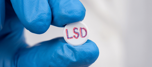 Person in Handschuhen hält 1D-LSD Pellet mit LSD-Aufschrift vor weißem Hintergrund